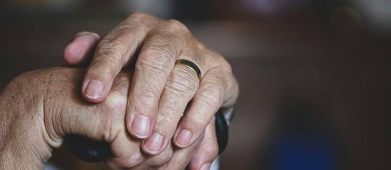An older adult's hands resting on a cane